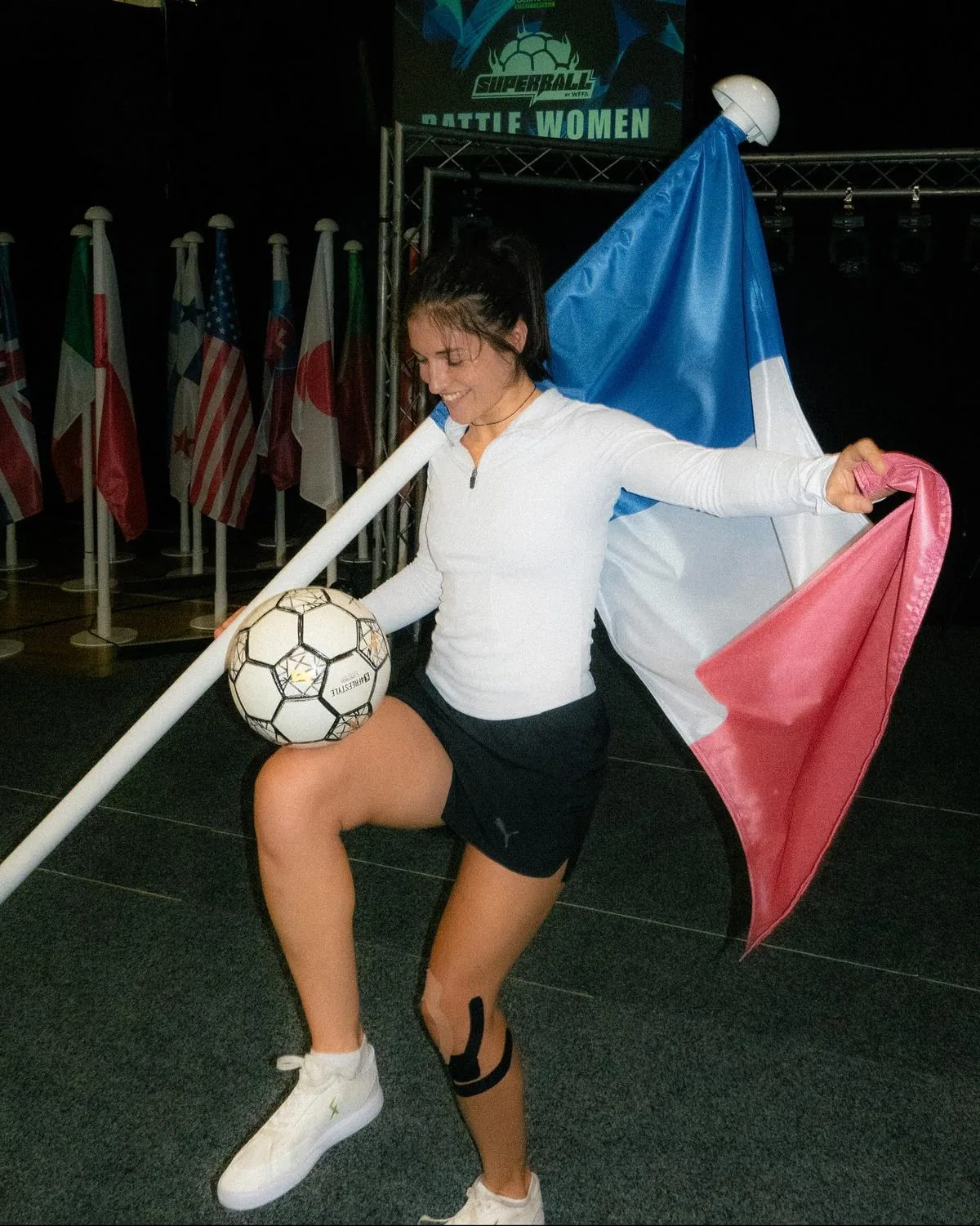 Yoanna Dallier jongle, le drapeau français sur les épaules, devant les drapeaux des nations